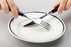 Hungry person hand holding fork knife on food plate