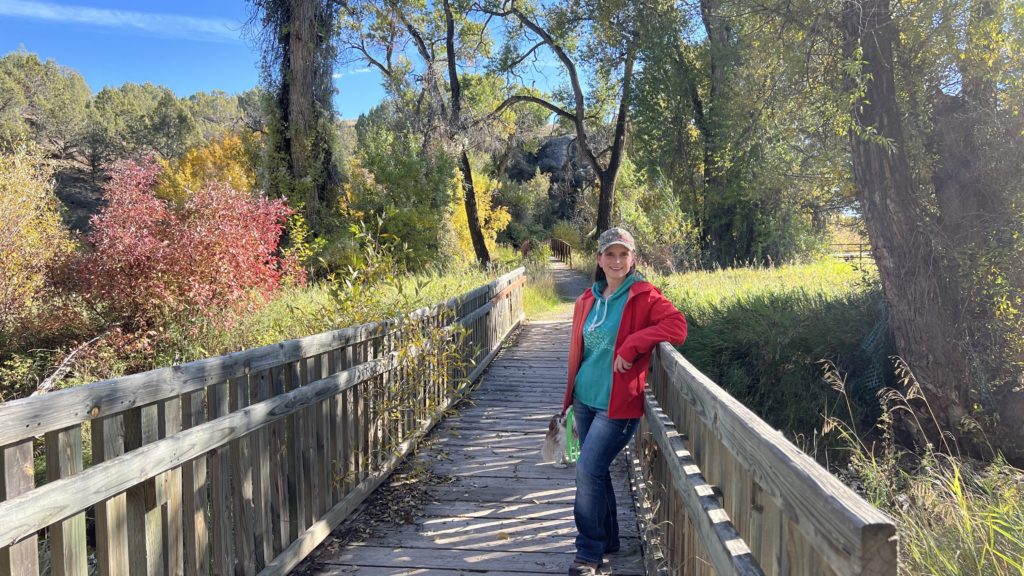 Melissa Cook stands on a wooden bridge surrounded by fall colors in the background.
