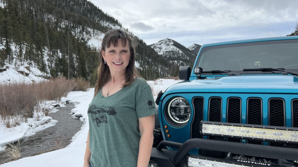 Melissa Cook standing in front of her blue Jeep by a icy river