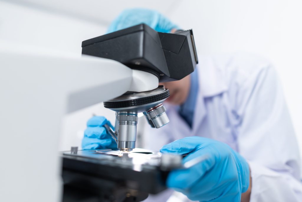 Scientist looking into a microscope with blue gloved hands holding and manipulating the test