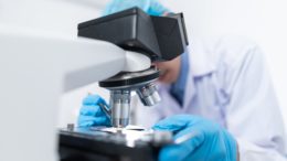 Scientist looking into a microscope with blue gloved hands holding and manipulating the test